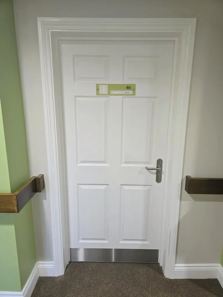White room door with number sign and metal kick plate in corridor with coloured wall finish
