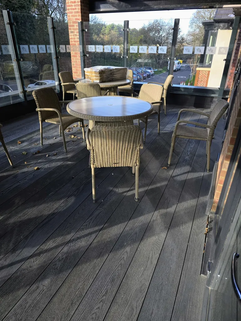 Outdoor terrace with round table and wicker chairs on composite decking with glass balustrade