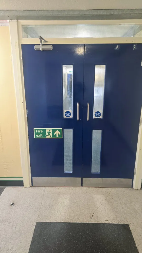 Double blue fire exit doors with vertical vision panels and overhead door closer