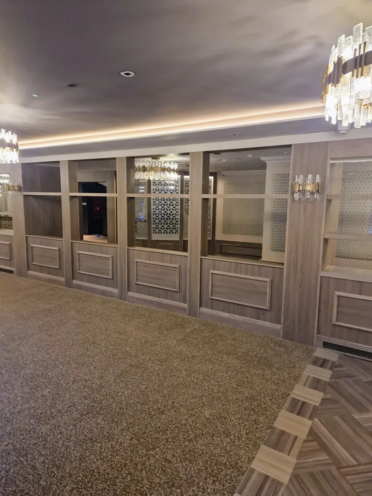 Wall panelling with inset shelving and mirrored sections in a carpeted lounge space