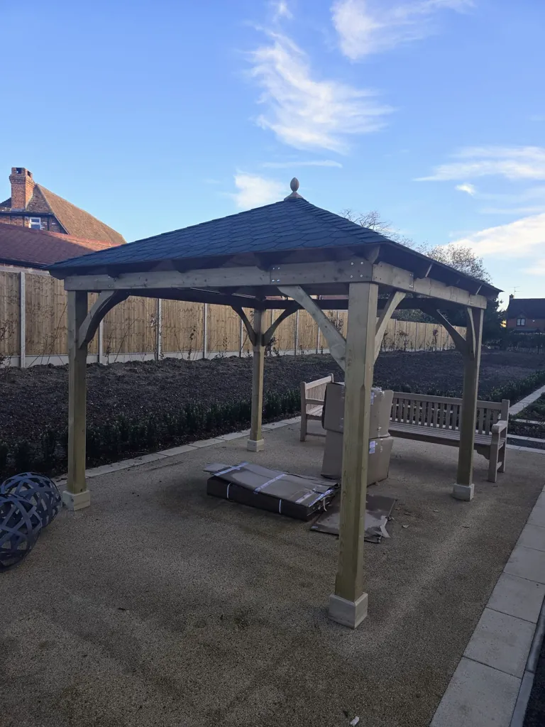 Wooden gazebo with pitched roof covering outdoor seating area on landscaped ground