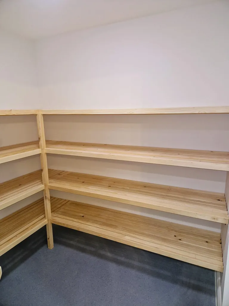 Long run of wooden batten shelves mounted along wall in storage room