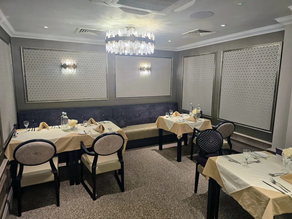 Dining room with set tables, upholstered chairs, wall panelling and central chandelier lighting