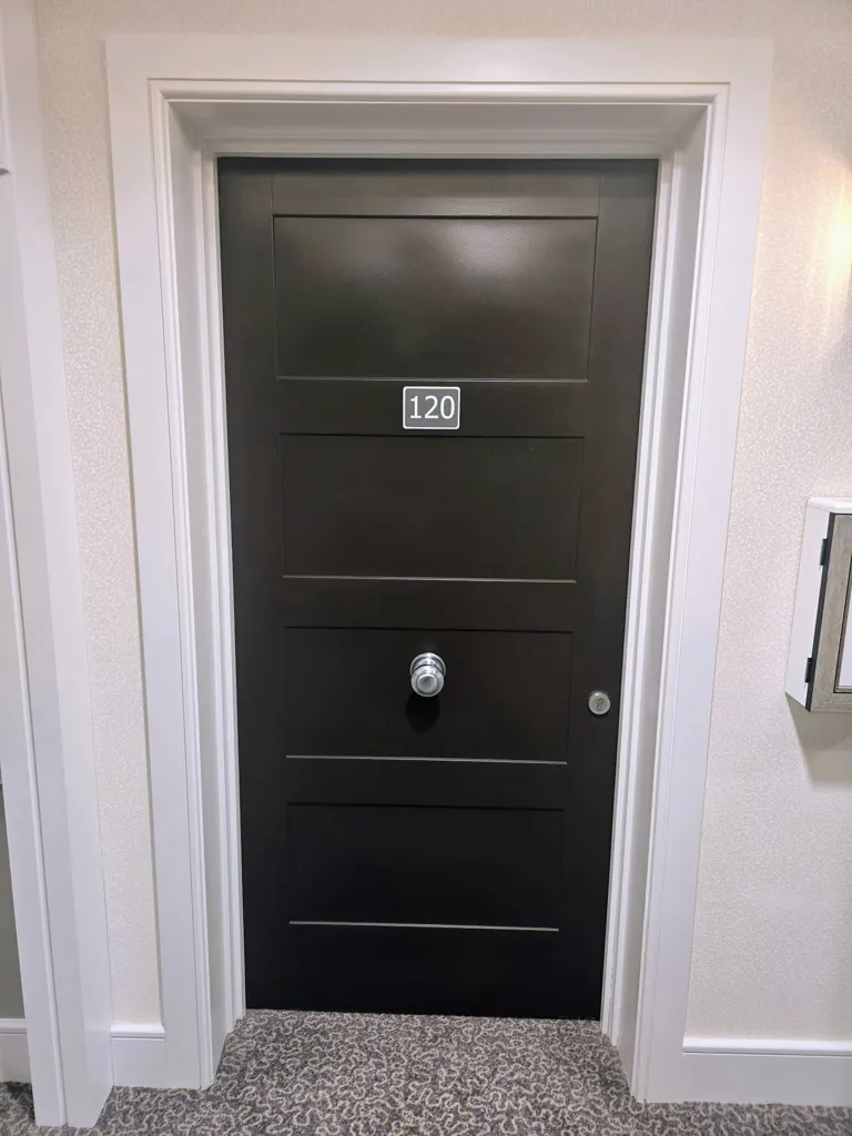 Dark entrance door with room number plaque and peephole set within white frame