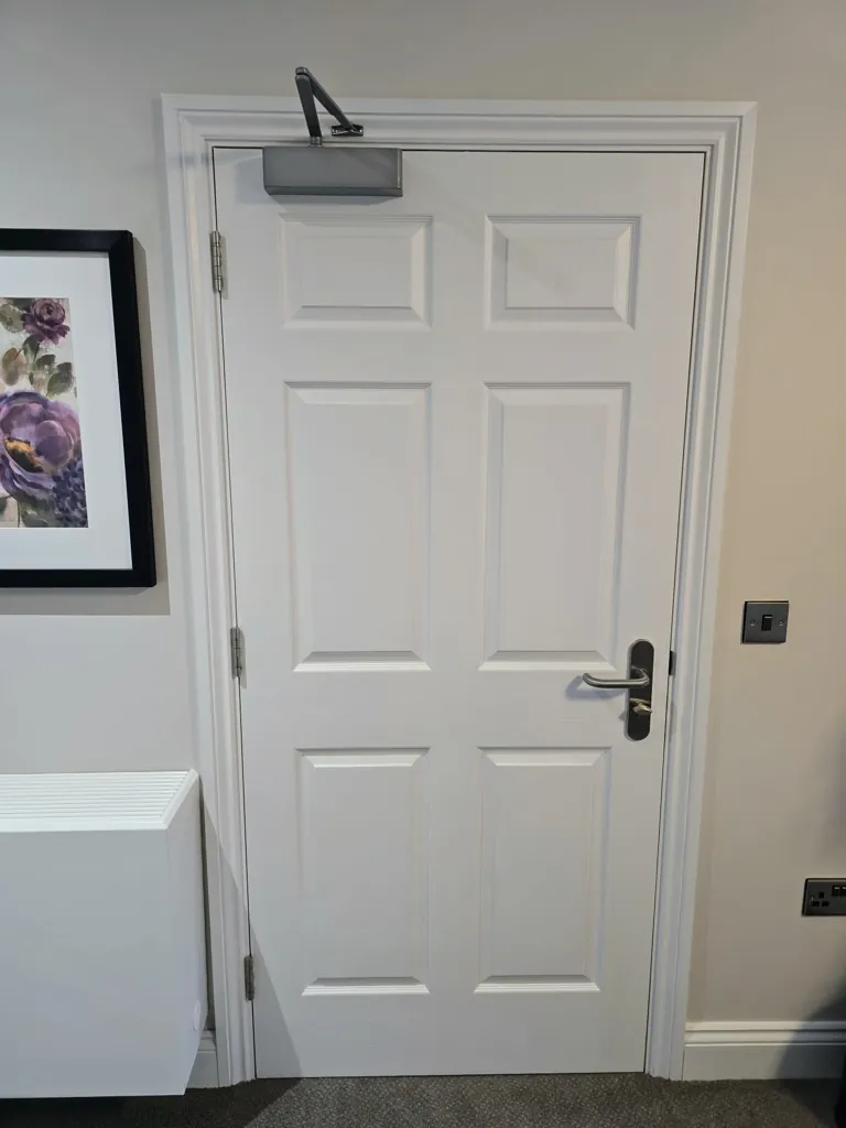 White panel door with overhead door closer and metal handle in interior setting