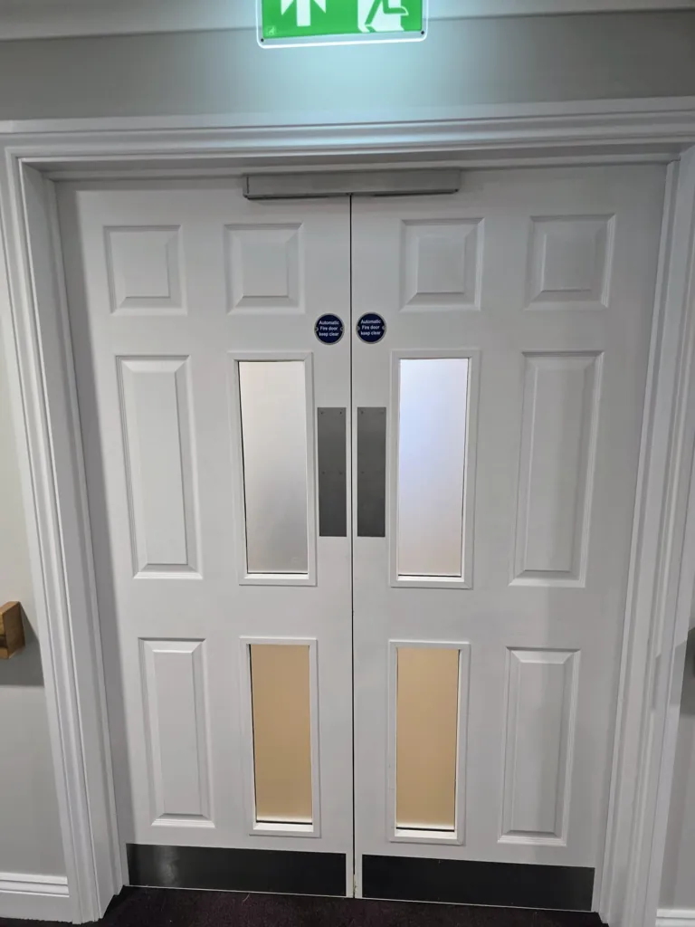 White double doors with vertical vision panels and illuminated exit sign above